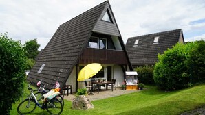 Une maison moderne avec un toit en pente, une terrasse avec une table et des chaises, et un vélo garé à l’extérieur.
