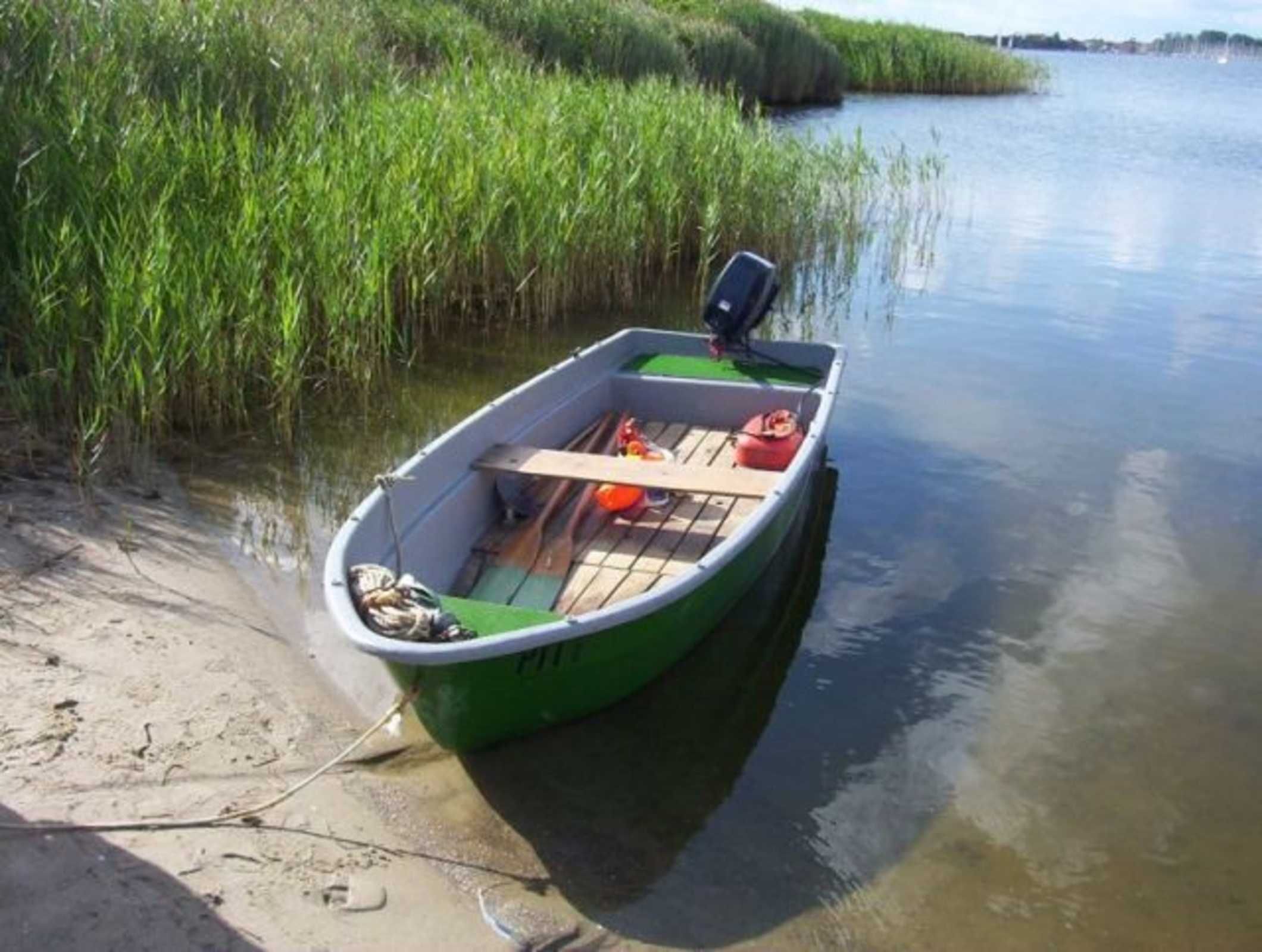A small green boat with a motor, wooden benches, and a red life jacket on the shore.