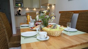Une table mise pour le petit-déjeuner, avec une table en bois, des chaises en osier, un panier de pain, un vase de fleurs et des aliments typiques du petit-déjeuner, comme des œufs et du jus de fruits.