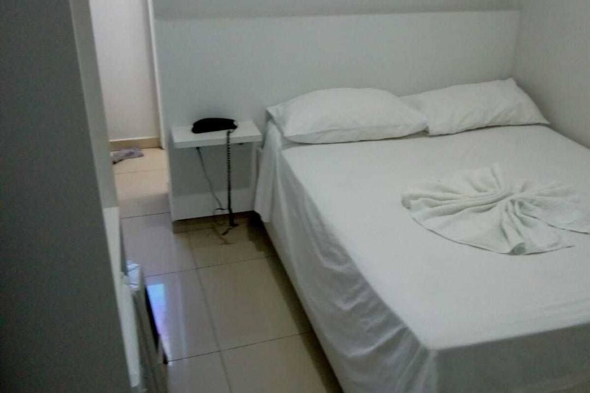 A small, single-bed room with a white bedspread, a bedside telephone, and a neatly folded towel on the bed.