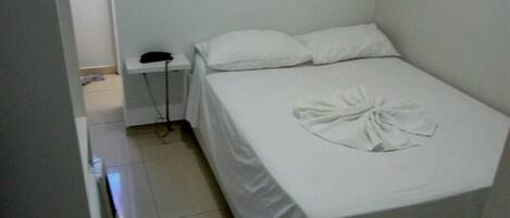 A small, single-bed room with a white bedspread, a bedside telephone, and a neatly folded towel on the bed.