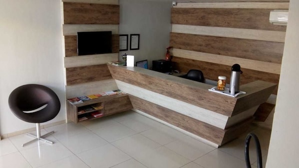 A reception desk with a wooden finish, a black chair, and a small shelf with magazines.