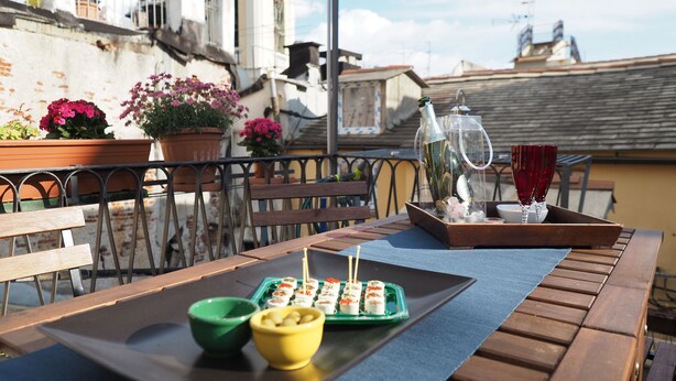 A wooden table with a tray of sushi, a green bowl, a yellow bowl, and a glass of red wine on a balcony with potted plants and a railing. - Caratteristica Dimora Della Galera (Genoa)