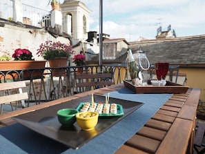 A wooden table with a tray of sushi, a green bowl, a yellow bowl, and a glass of red wine on a balcony with potted plants and a railing. - Caratteristica Dimora Della Galera (Genoa)