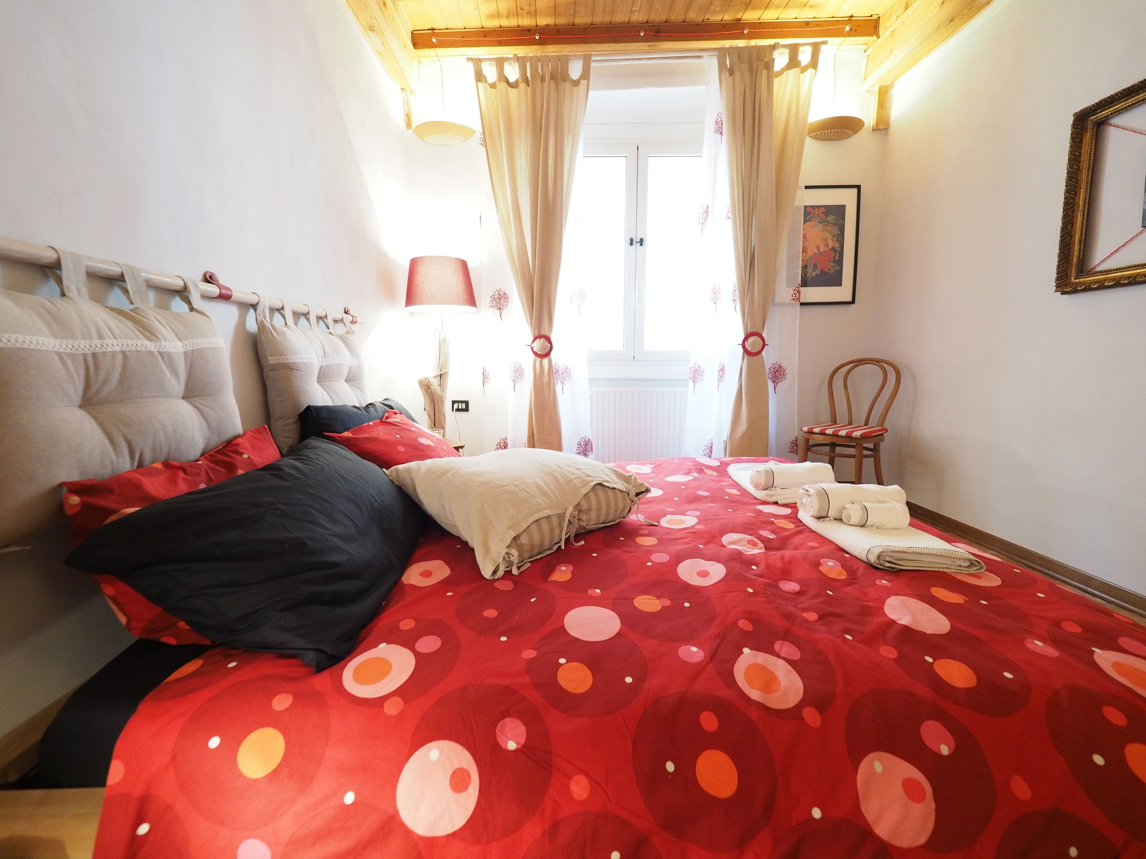 A bedroom with a bed, pillows, a chair, a lamp, and a window with curtains.