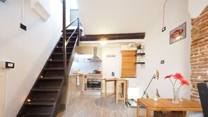 A modern kitchen with a wooden staircase, a dining area with a wooden table, and a brick wall. - Caratteristica Dimora Della Galera (Genoa)