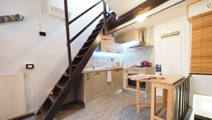 A kitchen with a wooden staircase, a dining table, and a sign indicating a bathroom. - Caratteristica Dimora Della Galera (Genoa)