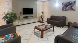 A living room with a sofa, a coffee table, a TV, and a plant. - Hotel Veneza (Brusque)