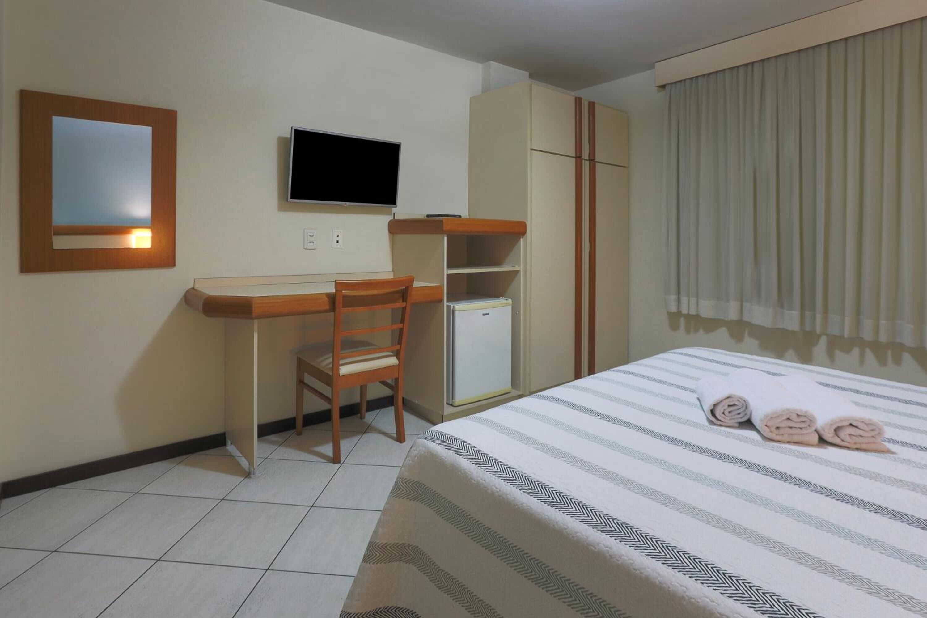 Une chambre d’hôtel comprenant un lit, un bureau avec une chaise, une télévision et une armoire.