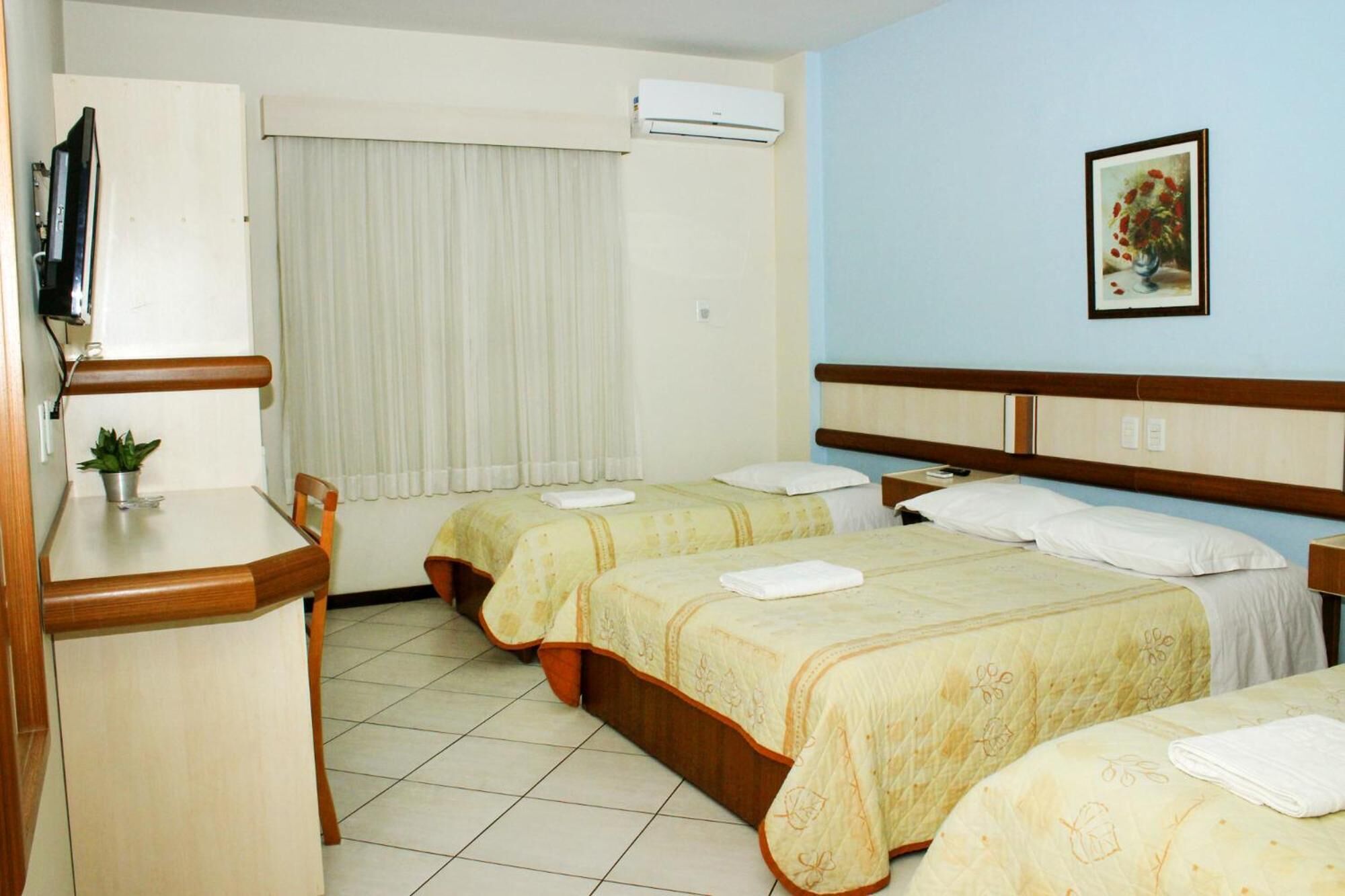 A hotel room with two beds, a desk, a chair, a TV, and a painting on the wall.