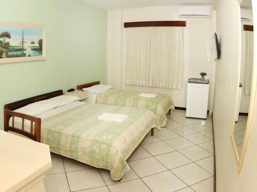 Habitación de hotel con dos camas, un escritorio pequeño, un refrigerador y un cuadro en la pared.