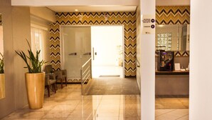 A hotel lobby with a reception desk, a coffee machine, and a large potted plant. - Hotel Veneza (Brusque)