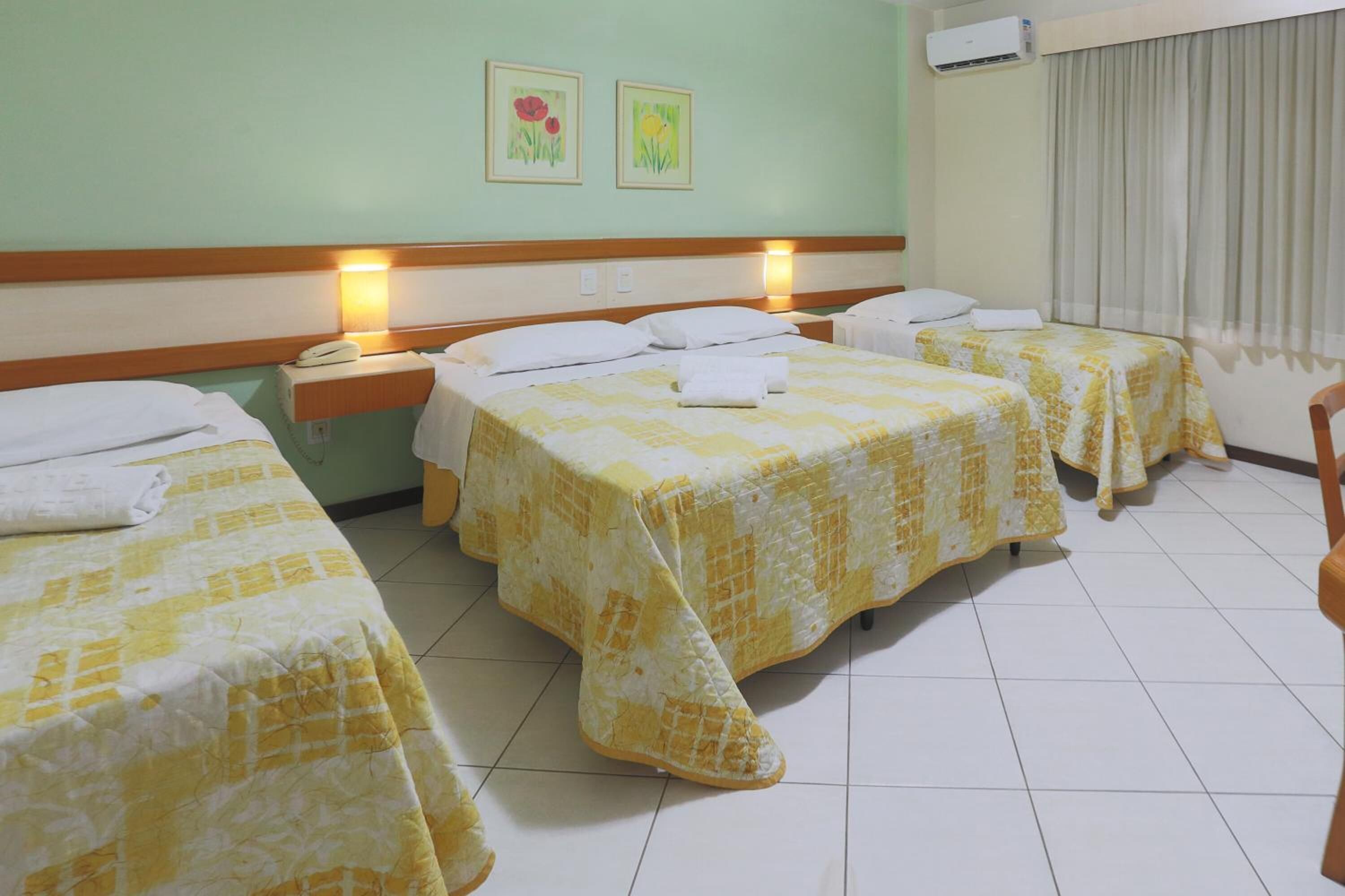 A hotel room with three beds, each with a yellow and white checkered bedspread, a wooden headboard, and a nightstand with a telephone.