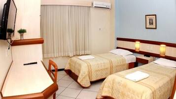 Habitación de hotel con dos camas, un escritorio, una silla, un televisor y aire acondicionado.