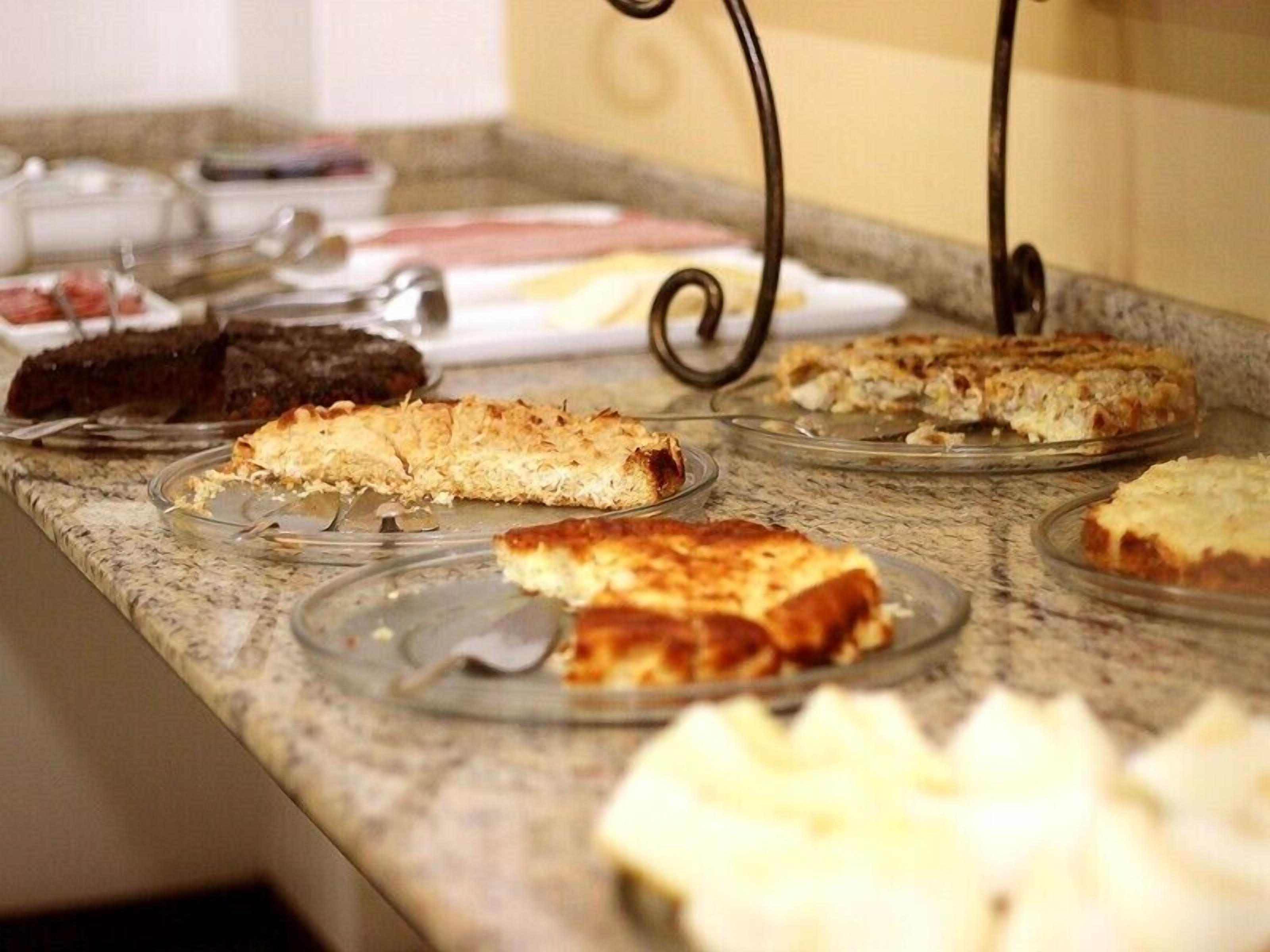 Mostrador de buffet con diversos platos, incluyendo porciones de pizza y otros productos horneados, sobre bandejas de vidrio.