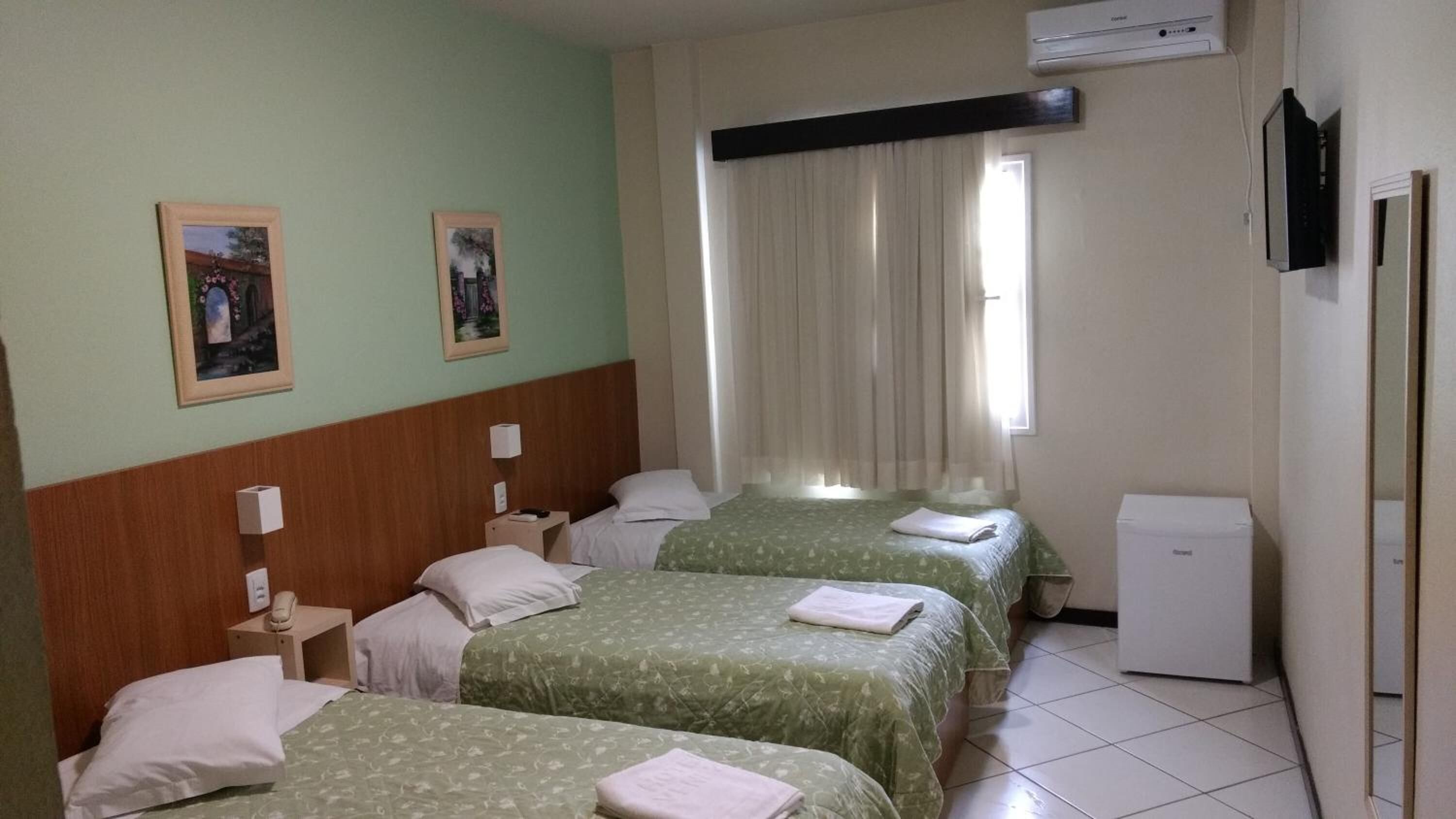 Habitación de hotel con dos camas, un escritorio pequeño, una silla, un televisor y una ventana con cortinas.
