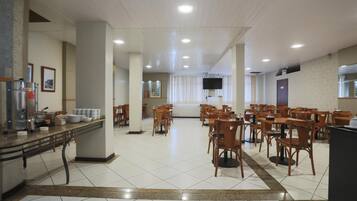 Un grand espace de salle à manger avec plusieurs tables et chaises, un comptoir équipé d’appareils de cuisine et un téléviseur fixé au mur.