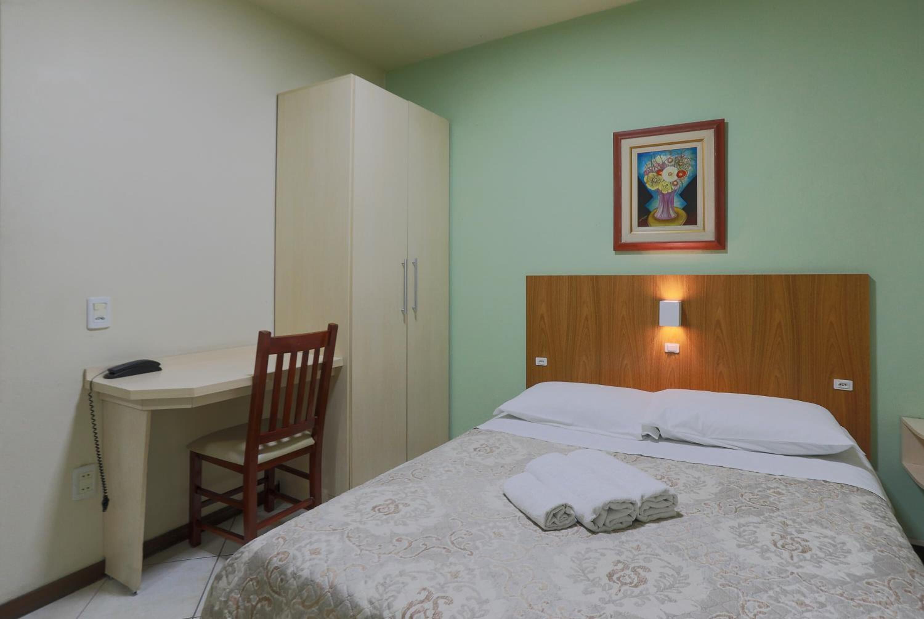 Een hotelkamer met een bed, een bureau, een stoel en een kledingkast.