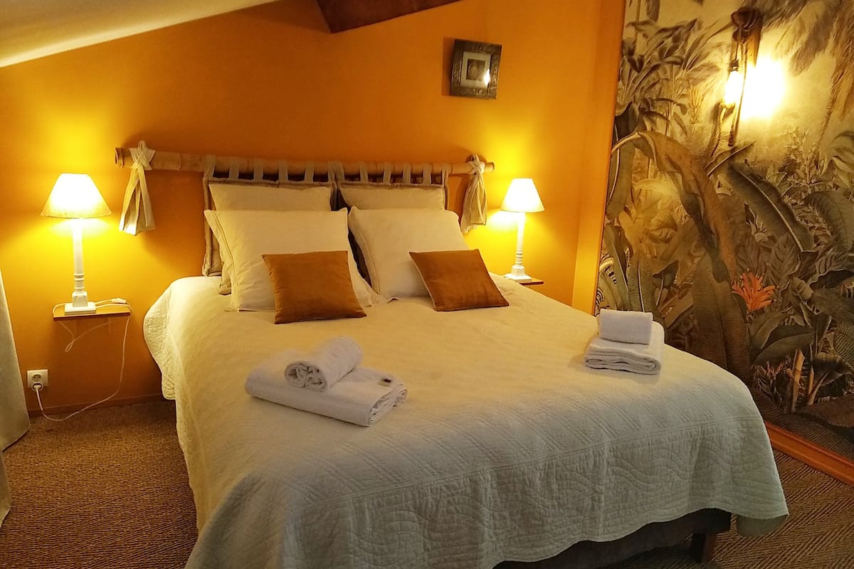A neatly made bed with pillows and a folded towel, two bedside lamps, and a tropical-themed wall mural.