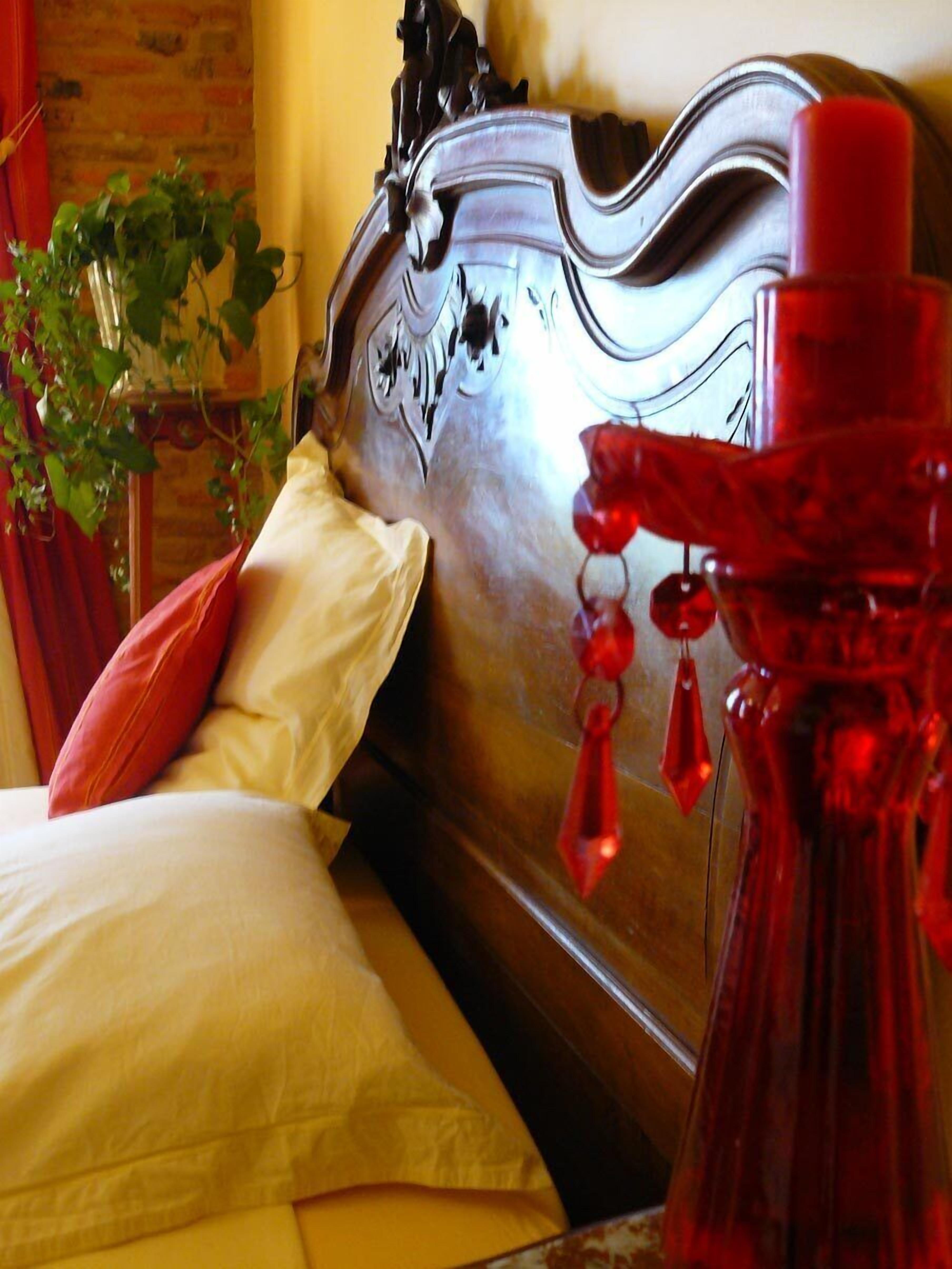 Una cama con cabecera de metal, una vela roja y una planta en maceta.
