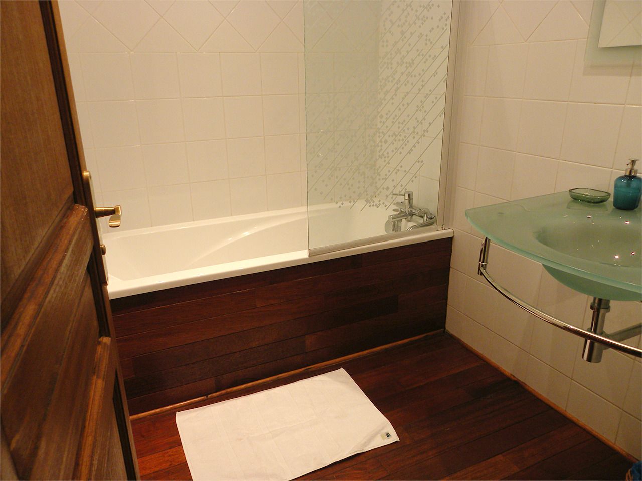 Une salle de bain avec une douche à l’italienne en verre, une baignoire blanche et un lavabo en verre avec un distributeur de savon bleu.