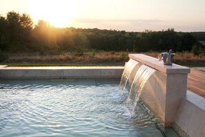 A pool with a waterfall feature, a metal bucket, and a glass on the edge. - Chambres d'Hotes Belair (Eaunes)