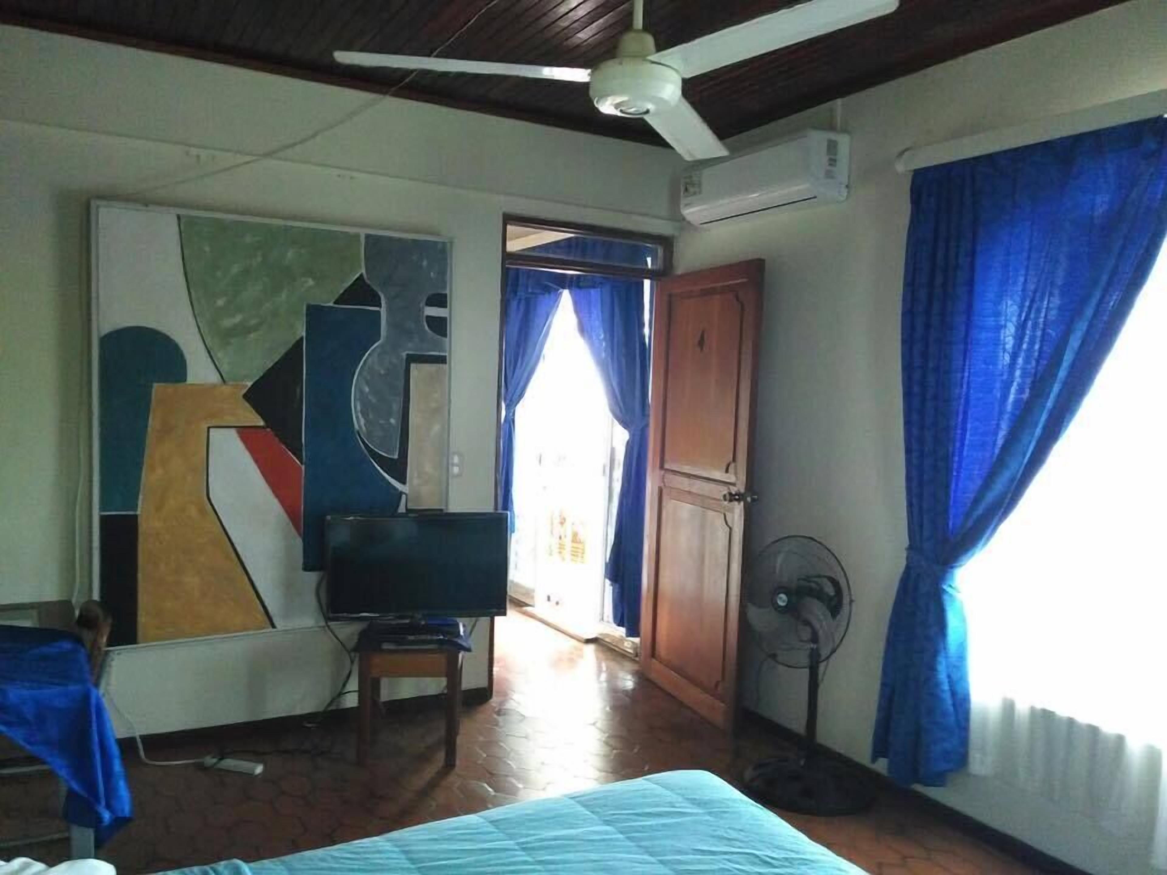 Een kamer met een bed, een televisie, een ventilator en een deur naar een andere kamer.