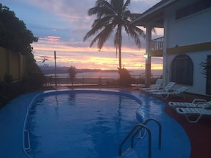 En pool med solstolar, utsikt över solnedgången och palmer.