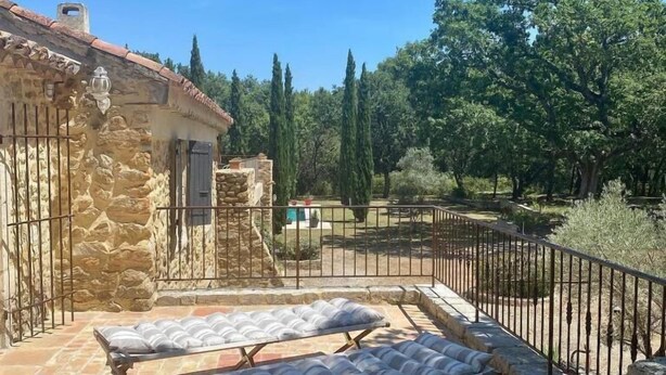 A stone building with a tiled roof, two lounge chairs, and a fenced garden area with trees and shrubs. - Domaine du Commandeur (Mondragon)