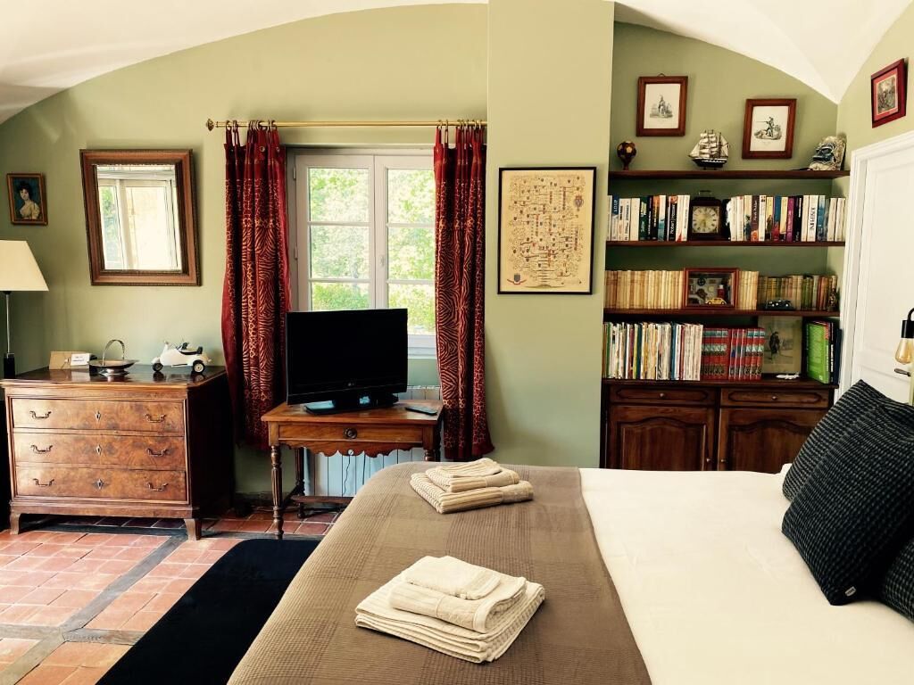 Une chambre à coucher avec un lit, une télévision, une bibliothèque et une fenêtre avec des rideaux.