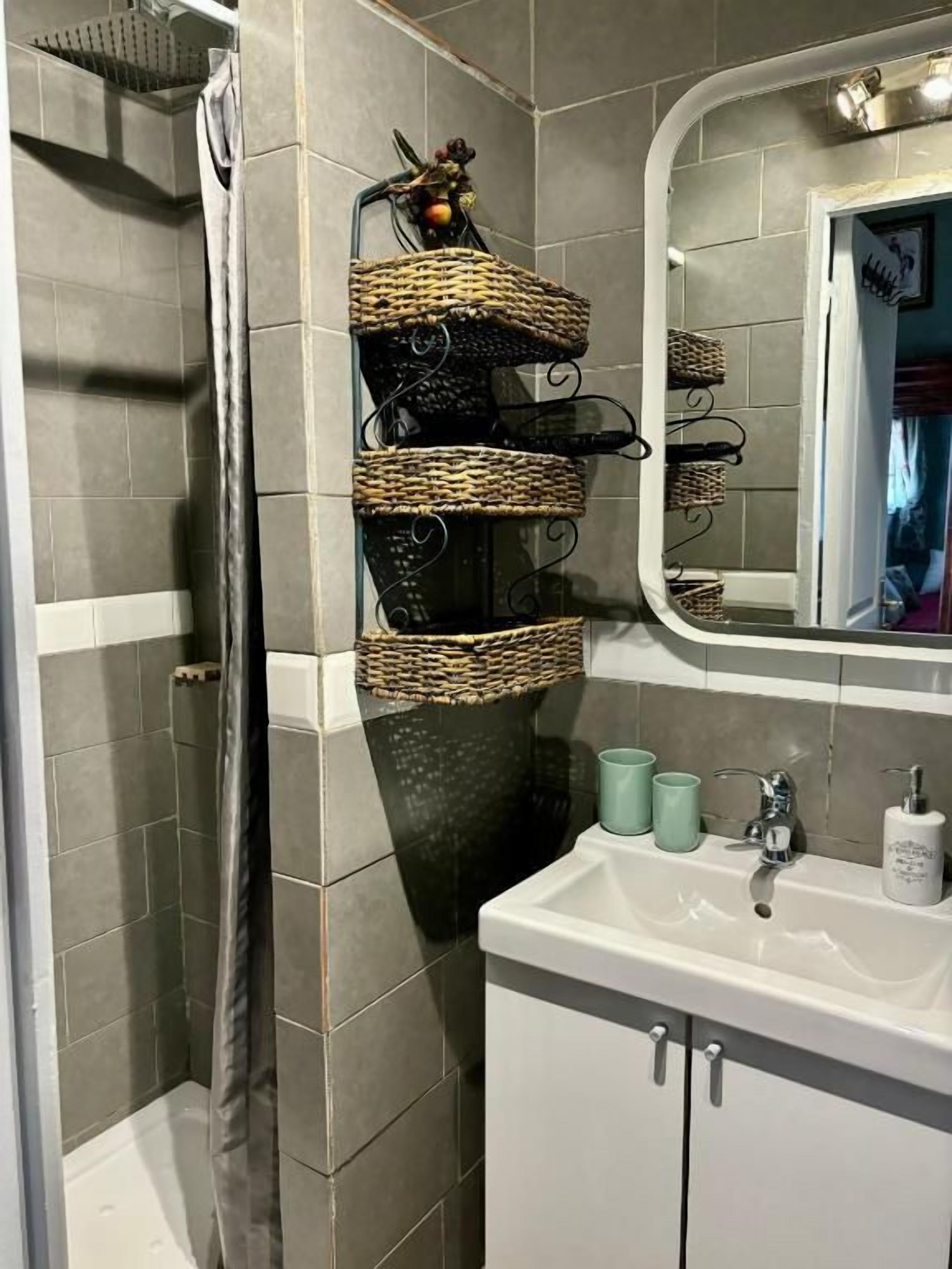 Une salle de bain avec une douche, un lavabo avec un miroir et des paniers en osier accrochés au mur.