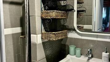 Une salle de bain avec une douche, un lavabo avec un miroir et des paniers en osier accrochés au mur.