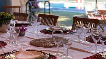 A table set for dining with multiple chairs, a view of the outdoors, and a pool in the background.