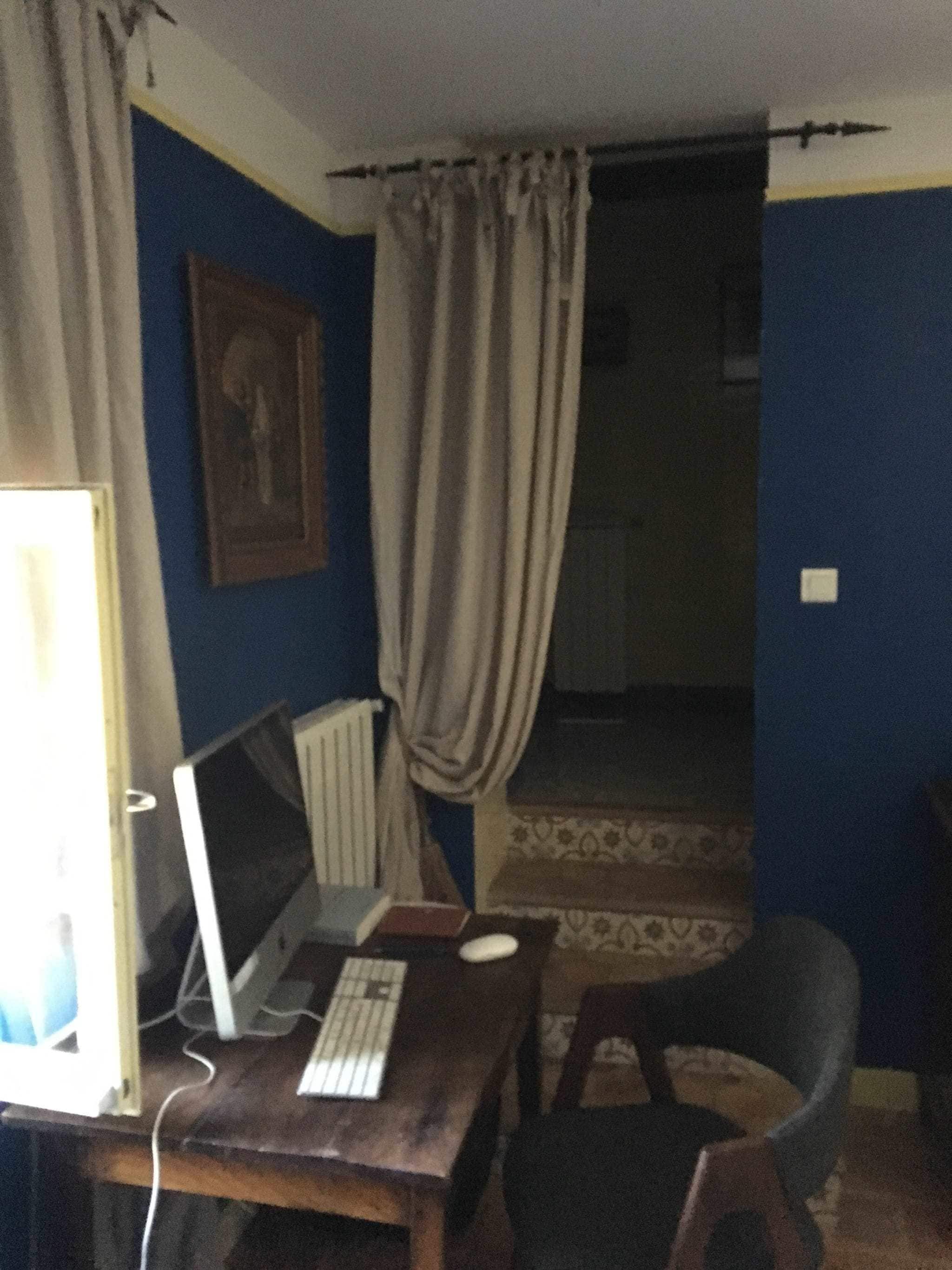 A room with a desk, computer, chair, and a window with curtains.