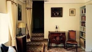 A cozy room with a chair, a small table with a lamp, a bookshelf, and a staircase with patterned tiles. - Domaine du Commandeur (Mondragon)