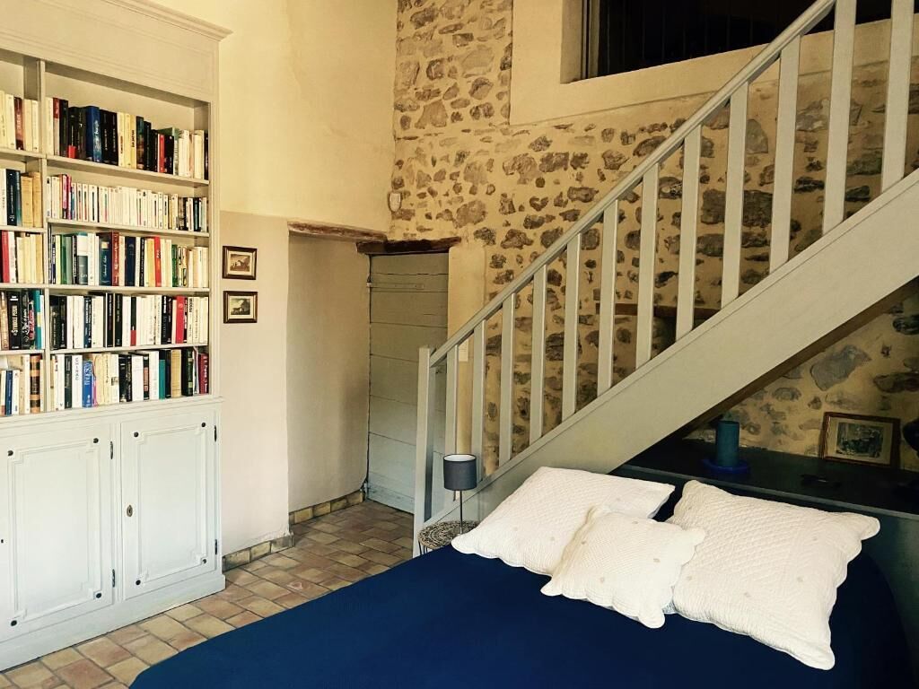 Une chambre avec un lit, une bibliothèque, un escalier et un mur en pierre.