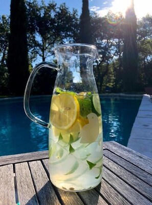A pitcher of lemonade with lemon slices and mint leaves, placed on a wooden table by a pool. - Domaine du Commandeur (Mondragon)