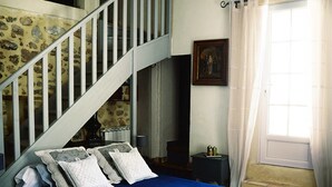 A bedroom with a bed, a staircase, a window with curtains, and a chair. - Domaine du Commandeur (Mondragon)