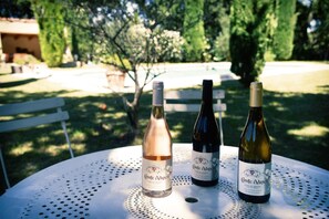 Three bottles of wine on a white table outdoors with a bench and trees in the background. - Domaine du Commandeur (Mondragon)