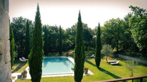 A pool surrounded by neatly trimmed grass and tall cypress trees, with lounge chairs and a stone wall in the background. - Domaine du Commandeur (Mondragon)