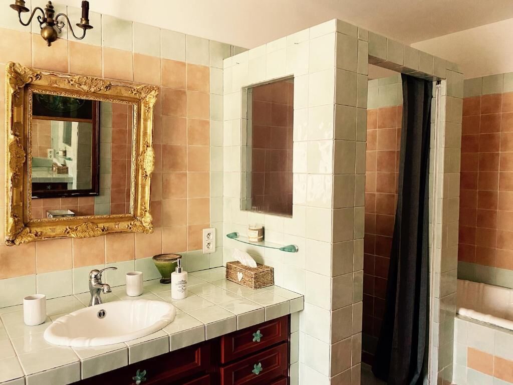 Een badkamer met een witte wastafel, een spiegel met een decoratief kader, en een douche met gordijn.