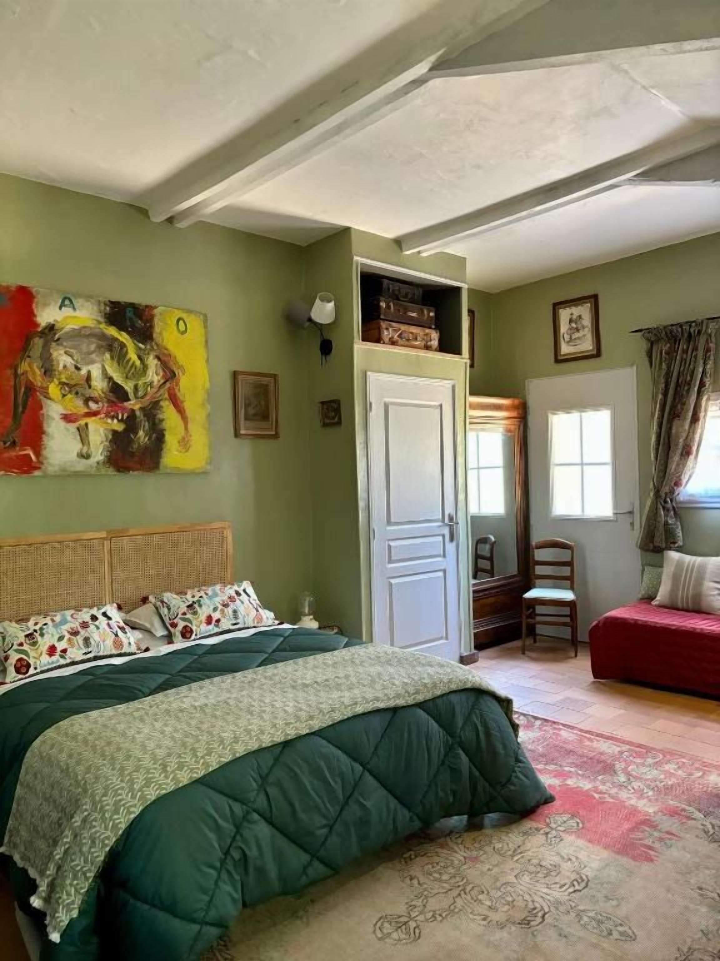 Une pièce avec un lit, une chaise, une porte et un tableau au mur.
