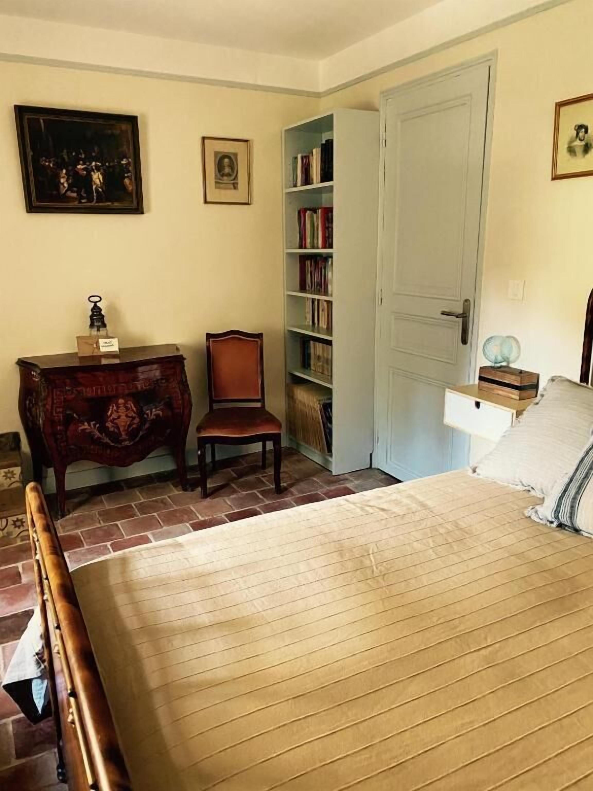 Un dormitori amb un llit i un taulell de fusta, una cadira, una prestatgeria i una porta.