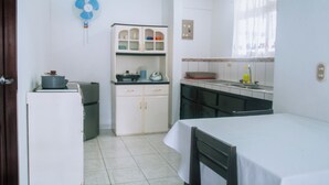 Eine kompakte Küche mit weißen Schränken, einem kleinen Kühlschrank und einem Essbereich mit Tisch und Stühlen.