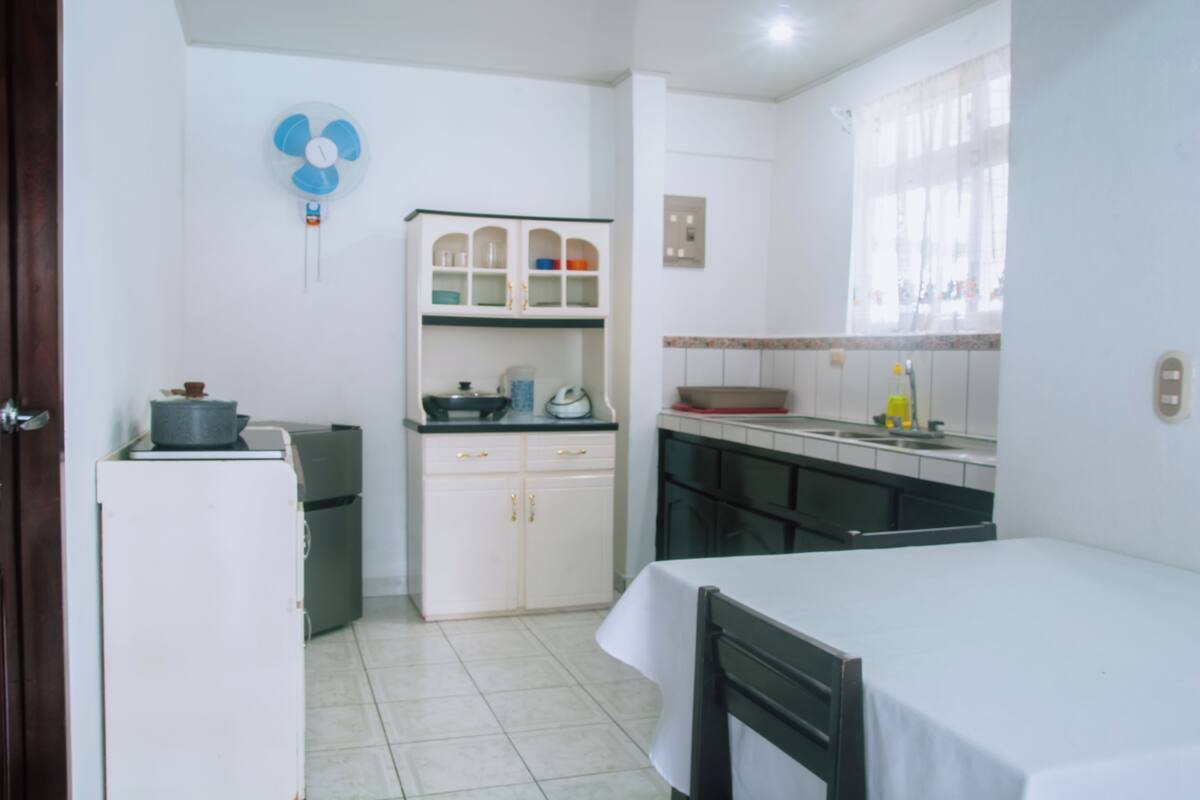 Une cuisine compacte avec des meubles blancs, un petit réfrigérateur et un coin repas comprenant une table et des chaises.