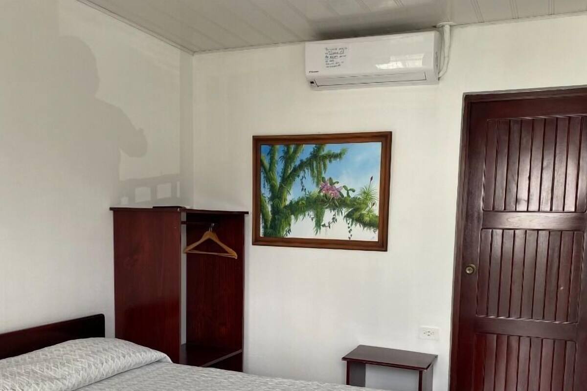 Une chambre à coucher comprenant un lit, une armoire, une petite table, une porte et un climatiseur fixé au mur.