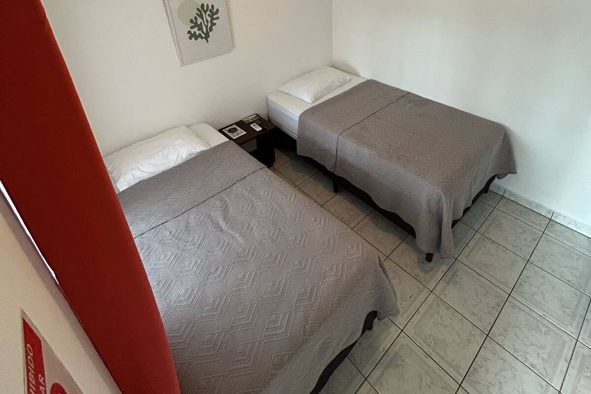 Une chambre avec deux lits simples, un luminaire au plafond, un climatiseur et un tableau encadré au mur.