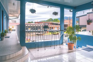 Ein Balkon mit Blick auf Gebäude und Berge, üppigen Pflanzgefäßen und einem gefliesten Boden.