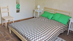 Un dormitorio con cama de madera, almohadas verdes, una mesita de noche con lámpara, una silla y un espejo en la pared.