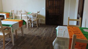 Un comedor con mesas y sillas de madera, una puerta de madera oscura y un suelo de tonos claros.